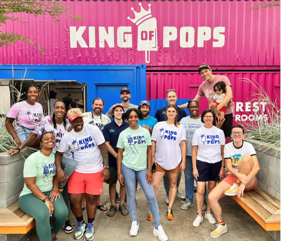 A crew of people wearing King of Pops t-shirts stand in front of a King of Pops storefront.