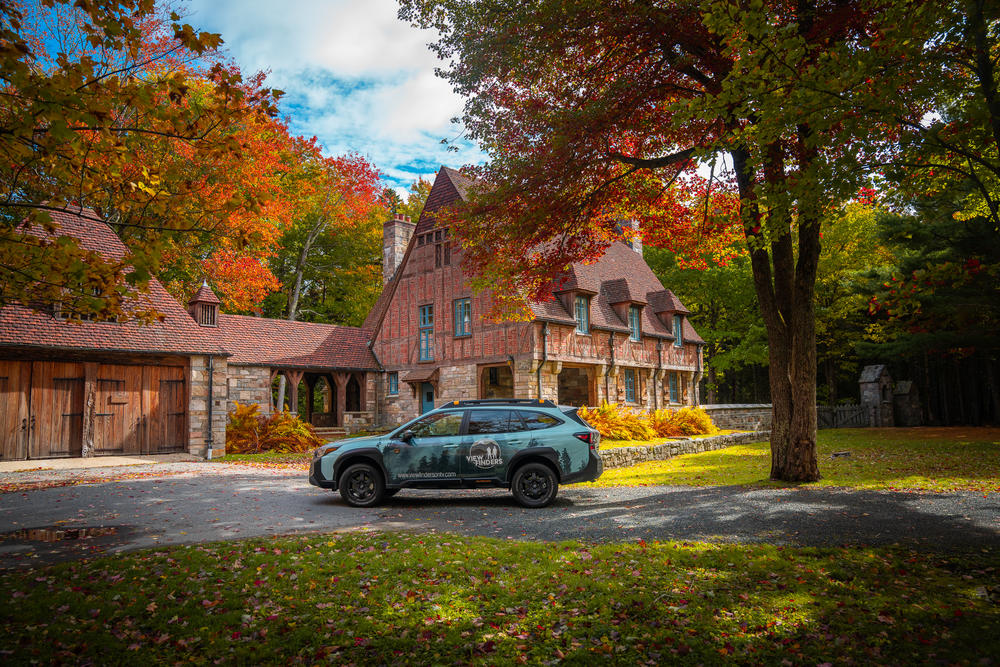 The View Finders car parked outside of a house surrounded by trees with changing autumn leaves