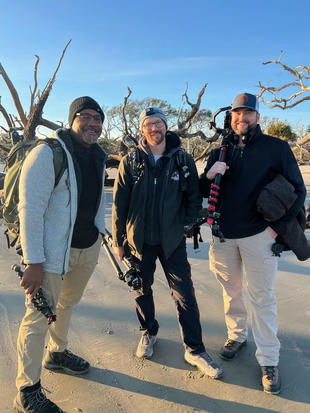 Three men pose in front of a large piece of driftwood in Golden Isles, Georgia