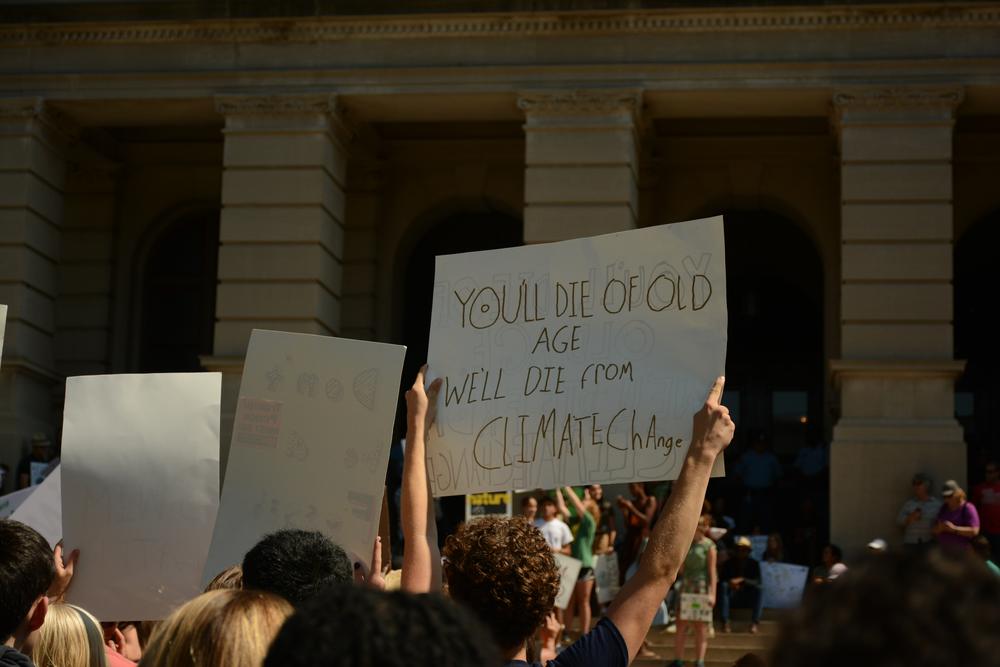 A students holds a sign on the steps of the capitol in Atlanta calling on leaders to take a stand against climate change.