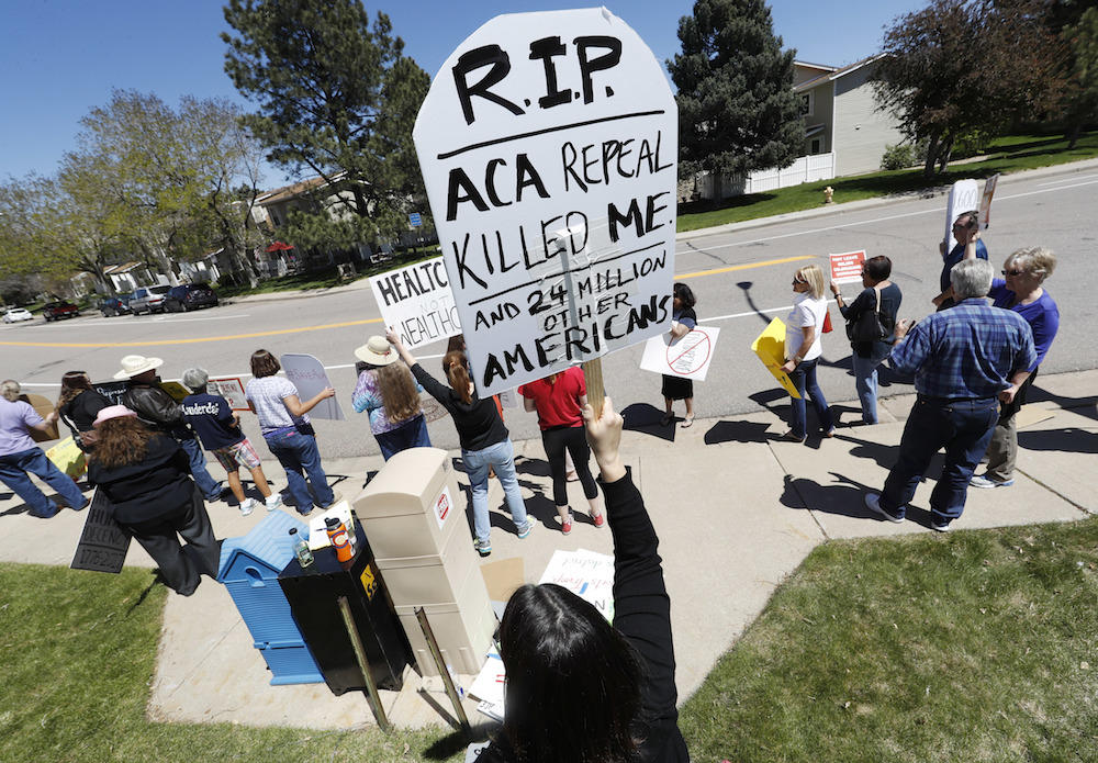 Lisa Moore of Denver holds up a sign during a protest outside the office of U.S. Rep. Mike Coffman, R-Colo., over the health care overhaul bill up for a vote in the U.S. House Thursday, May 4, 2017, in Aurora, Colo.
