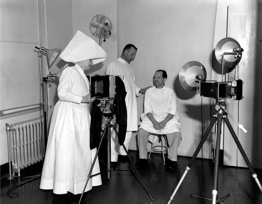 Sister Hilary Ross takes photos documenting a patient's treatment progress in the infirmary at the leprosarium in Carville, circa 1950. The photo was taken by Johnny Harmon, a patient with leprosy, for <em>The Star</em><em>, </em>a magazine for the residents at Carville.