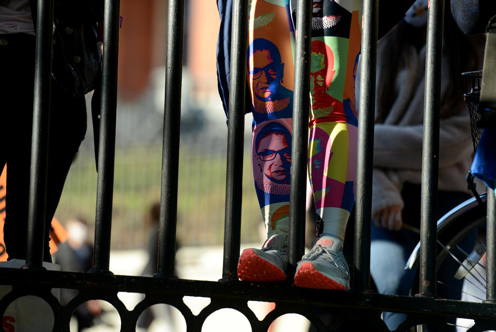 A woman wearing leggings featuring former Supreme Court Justice Ruth Bader Ginsburg scales a fence along the Boston Common.