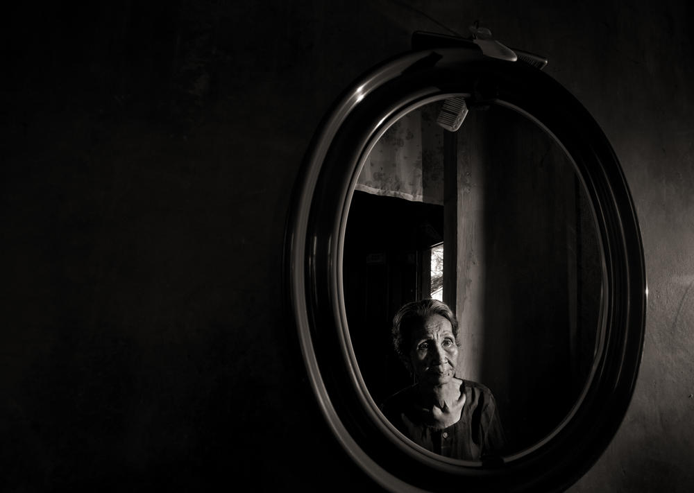 Emilia dela Cruz Mangilit is reflected in a mirror in her home in the village of Mapaniqui. Mangilit was only 15 years old when her village was shelled, then attacked by the Japanese during World War II.