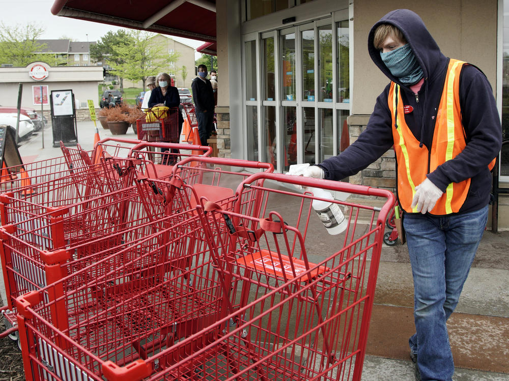 A Trader Joe's worker disinfects shopping carts and controls the number of customers allowed to shop at one time in Omaha, Neb., on May 7, 2020. Grocers like Trader Joe's are offering pay incentives to encourage their workers to get vaccinated against COVID-19.