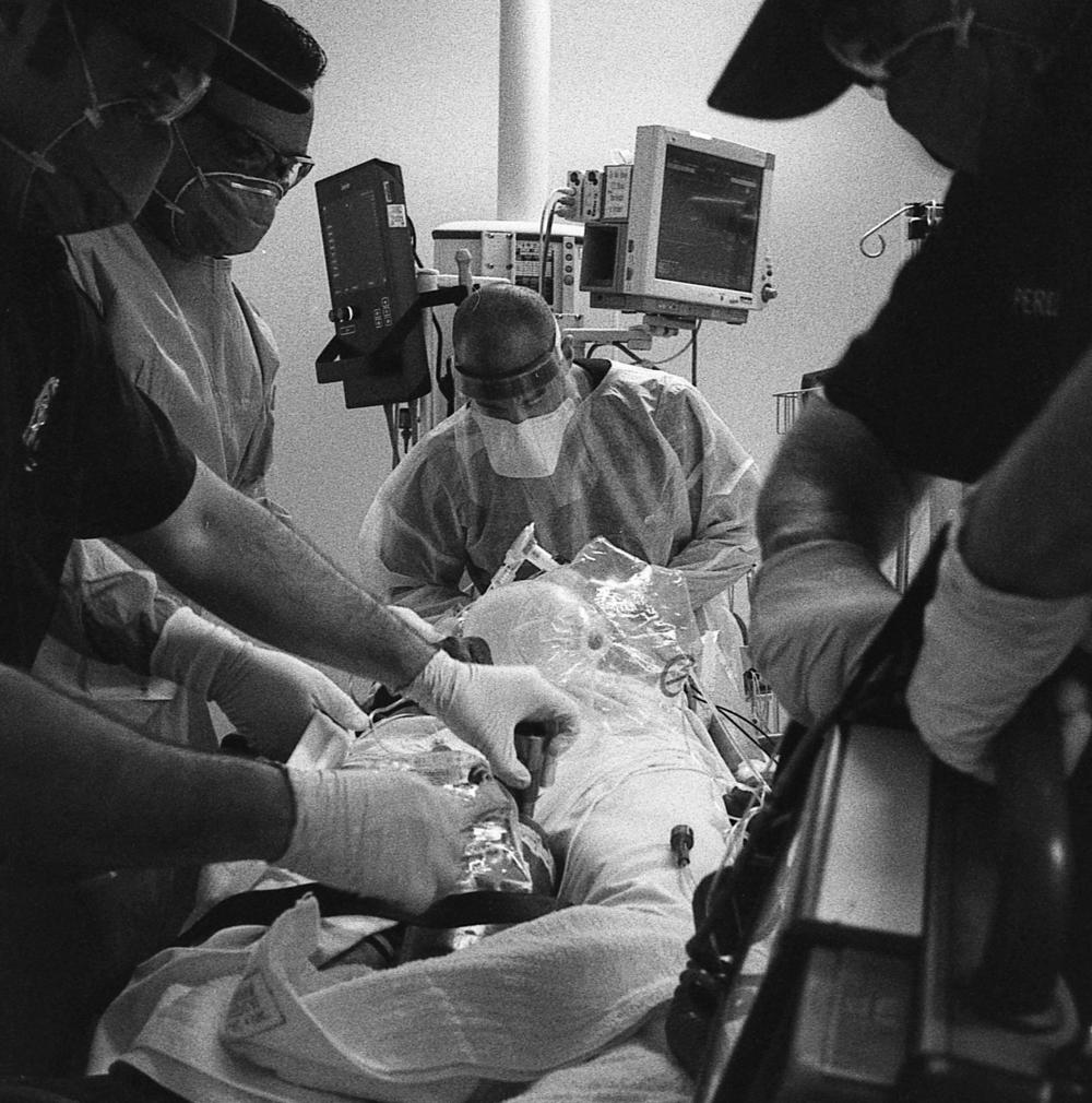 Dr. Brett Barro stands at the head of a COVID-19 patient's bed to speak with him. At home, the patient became rapidly hypoxic (their body lacked adequate oxygen) and now would require intubation for a chance at survival.