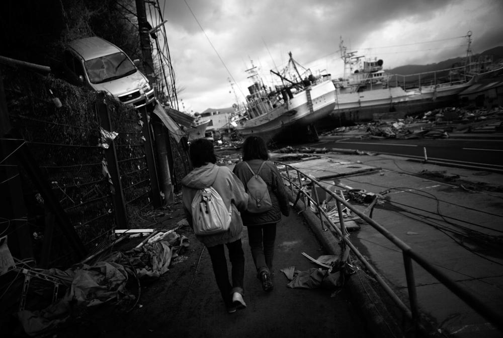 Two Japanese women walk through a neighborhood where cars and boats had been tossed around, in Kesennuma, Miyagi Prefecture, on March 22, 2011.