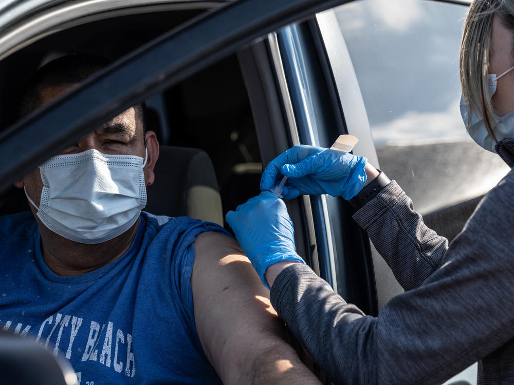A medical professional from UofL Health administers a vaccine to a patient in their vehicle at University of Louisville Cardinal Stadium.