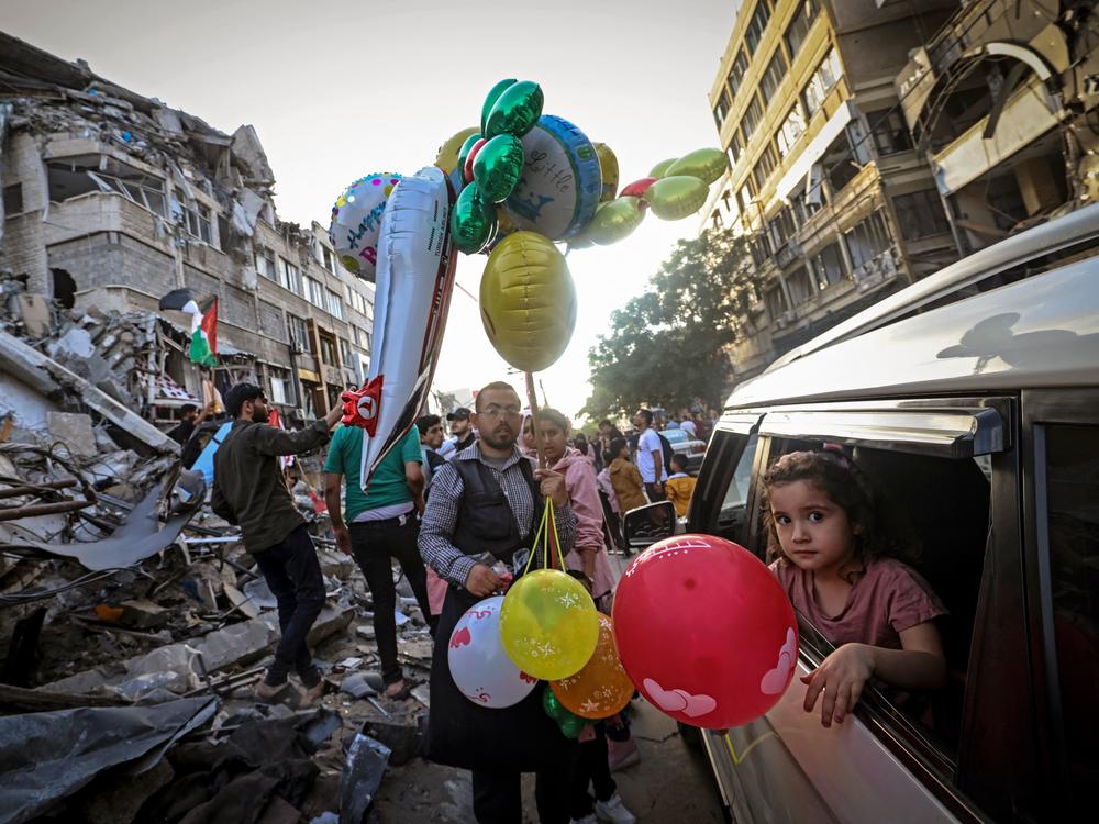 A Palestinian man sells balloons on Friday in Gaza City in front of the Al-Shuruq building, which was destroyed by an Israeli air strike.
