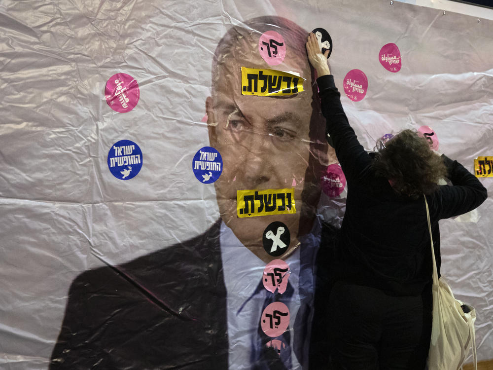 An Israeli protester places a sticker on a banner showing Israeli Prime Minister Benjamin Netanyahu during a demonstration outside the prime minister's residence in Jerusalem on June 5. The Hebrew reads: 