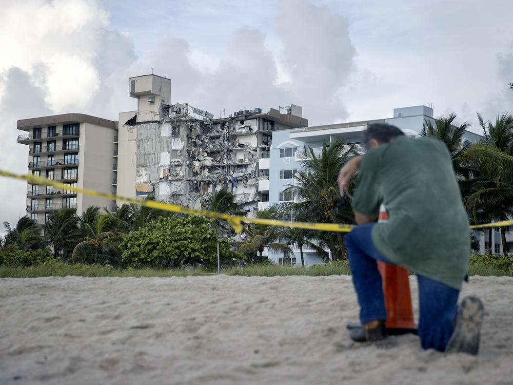 A man prays Friday near where search and rescue operations are ongoing at the partially collapsed 12-story Champlain Towers South condo building in Surfside, Fla.