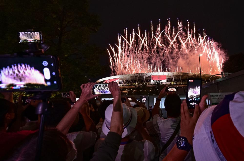 Supporters outside the Olympic Stadium take pictures of the fireworks lighting up the sky over Tokyo.
