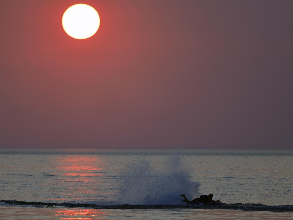 Western wildfires create a hazy sky as a person surfs on the water in Indiana Dunes State Park on Tuesday.