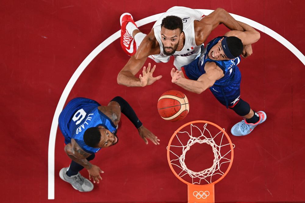 USA's Damian Lillard, left, looks on as teammate Devin Booker fights for a rebound with France's Rudy Gobert during the men's preliminary round group A basketball match between France and USA on July 25, 2021.