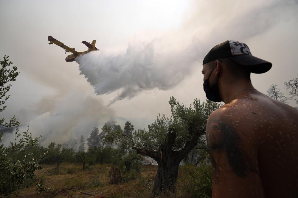 A local resident looks an aircraft dropping water over a wildfire at Ellinika village on Evia island, about 110 miles north of Athens, Greece, Monday, Aug. 9, Firefighters and residents battled a massive forest fire on Greece's second largest island for a seventh day, fighting to save what they can from flames that have decimated, vast tracts of pristine forest, destroyed homes and businesses
