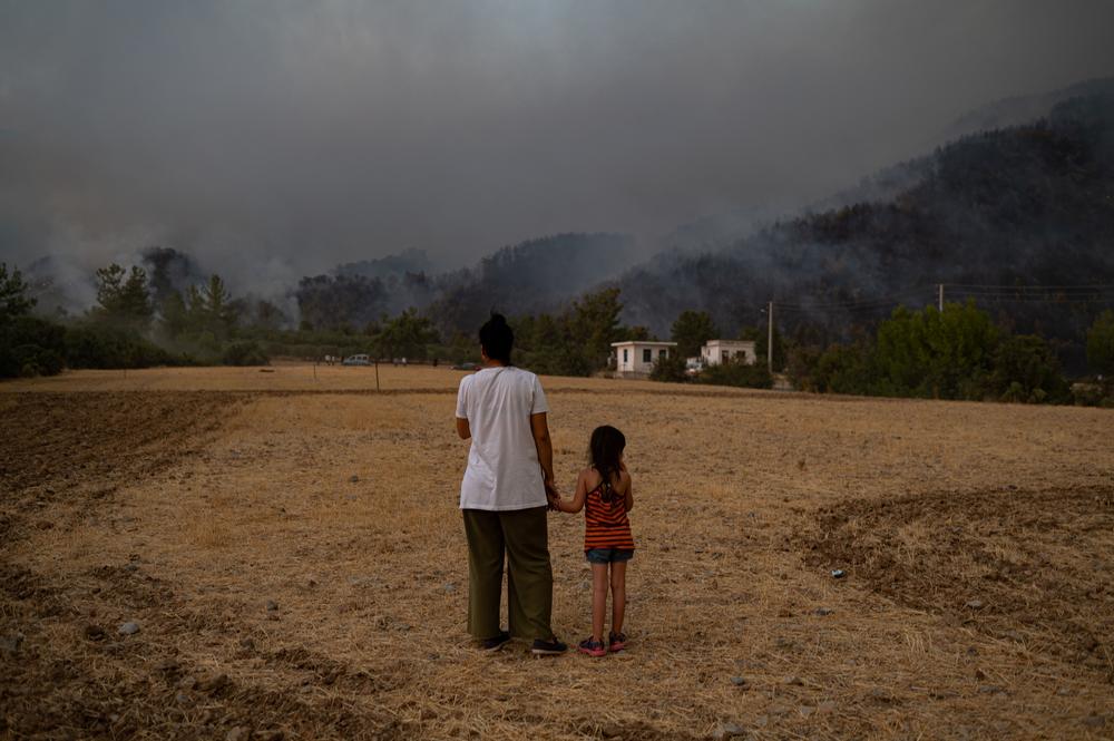 A woman and child stand in a field as they watch wildfires as they burn in Koycegiz district of Mugla on August 3, 2021. Turkey's struggles against its deadliest wildfires in decades come as a blistering heatwave grips southeastern Europe creating tinderbox conditions that Greek officials blame squarely on climate change.