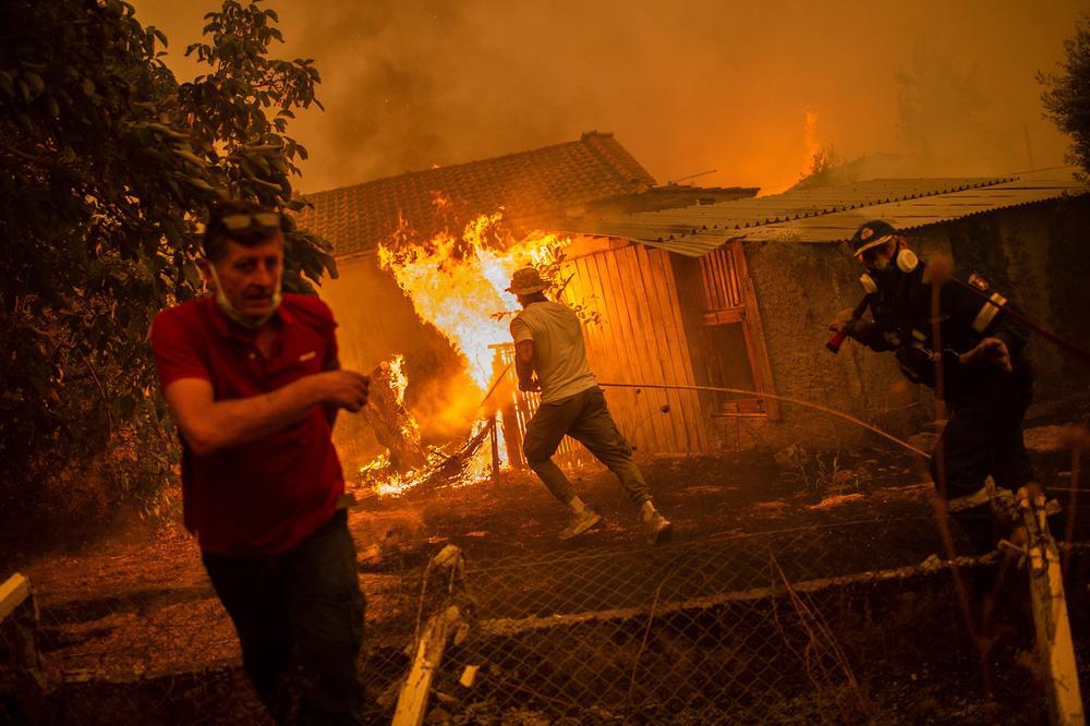 A firefighter and locals rush to a burning house in an attempt to extinguish forest fires that are approaching the village of Pefki on Evia (Euboea) island, Greece's second largest island, on August 8, 2021. Greece and Turkey have been battling devastating fires for nearly two weeks as the region suffered its worst heatwave in decades, which experts have linked to climate change.