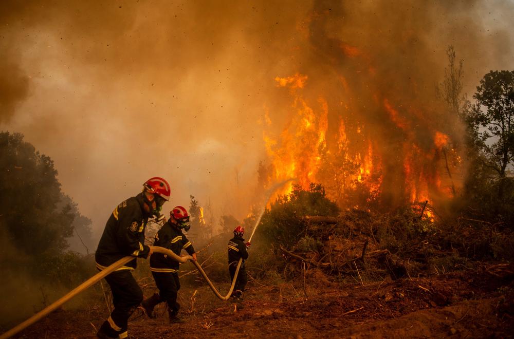 Serbian firefighters use a water hose to extinguish the burning blaze of a forest fire in the village of Glatsona on Evia (Euboea) island, on August 9, 2021.