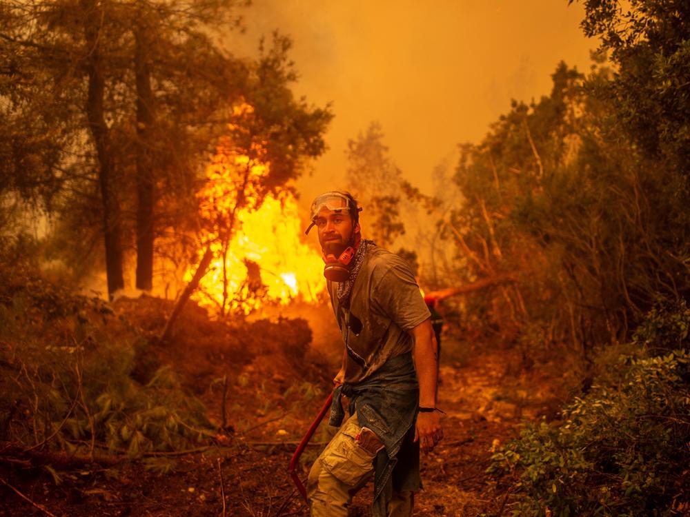 A volunteer holds a water hose near a burning blaze as he tries to extinguish a fire in the village of Glatsona on Evia (Euboea) island, on August 9, 2021. If most of nearly two weeks of fires had stabilised or receded in other parts of Greece, the ones on rugged and forested Evia were the most worrying and created apocalyptic scenes.