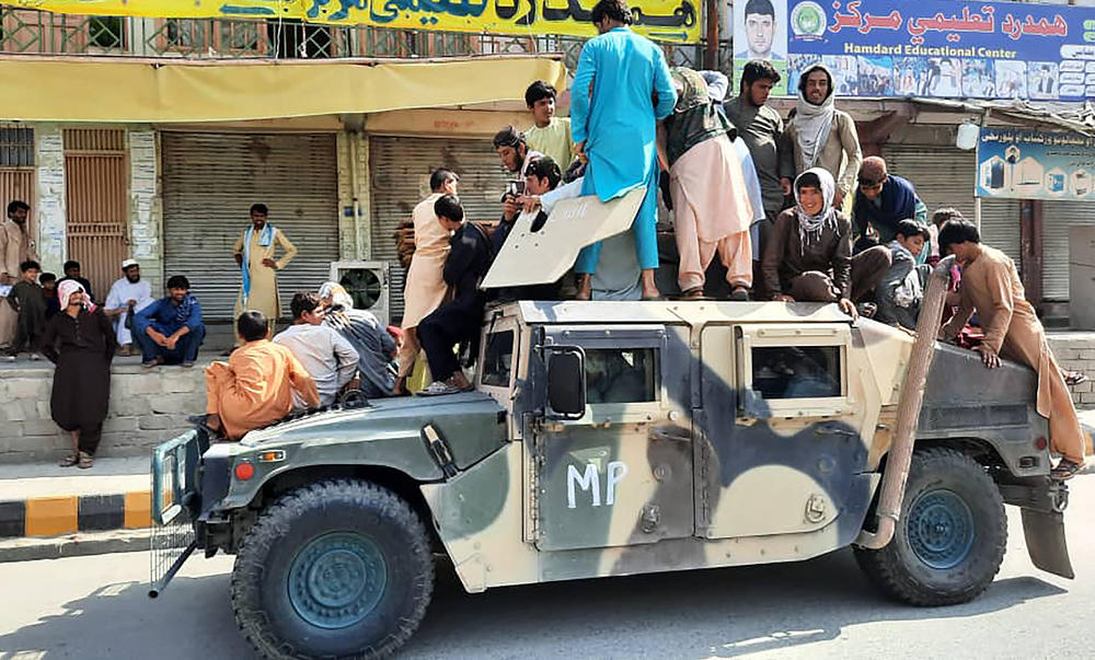 Sun., Aug. 15: Taliban fighters and local residents sit over an Afghan National Army humvee vehicle along the roadside in Laghman.