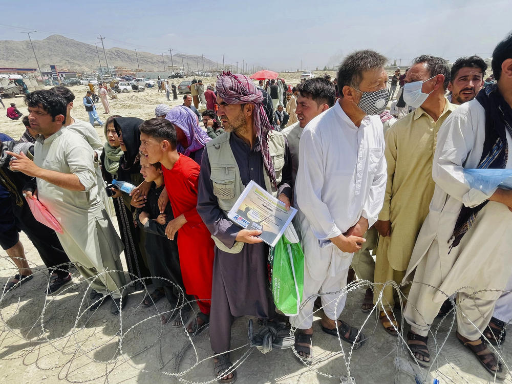 A man holds a certificate acknowledging his work for Americans as hundreds of people gather outside the international airport in Kabul, Afghanistan, Tuesday.