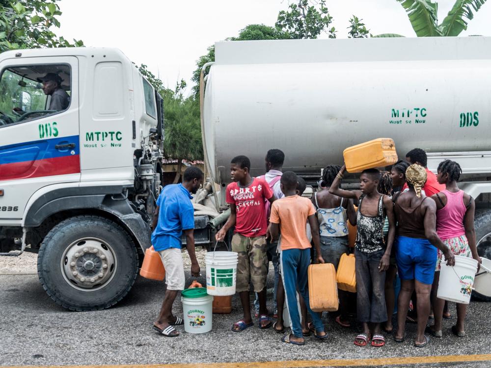 People gather near bins of water in Camp-Perrin, Haiti, on Monday.