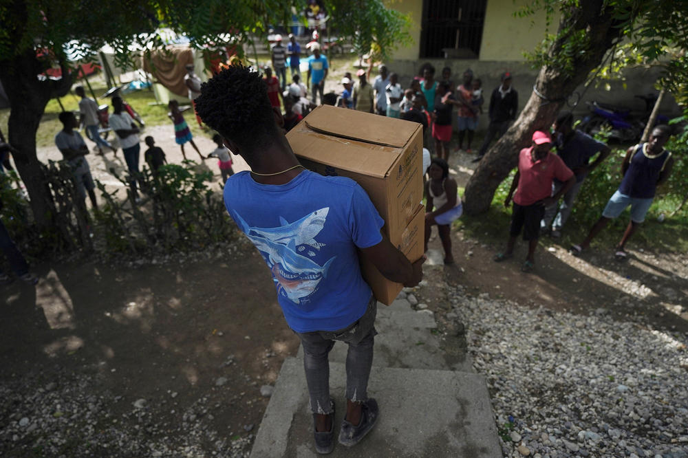 A man carries two of about 20 boxes of food aid from the city government to cook on site for residents displaced by the 7.2 magnitude earthquake staying in improvised tents next to a school in Les Cayes, Haiti, Wednesday, Aug. 18, 2021.