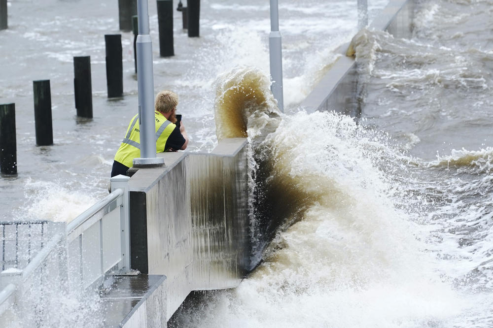 A utility worker photographs waves as they slam against a sea wall at the city marina as outer bands of Hurricane Ida arrive Sunday, in Bay Saint Louis, Miss.