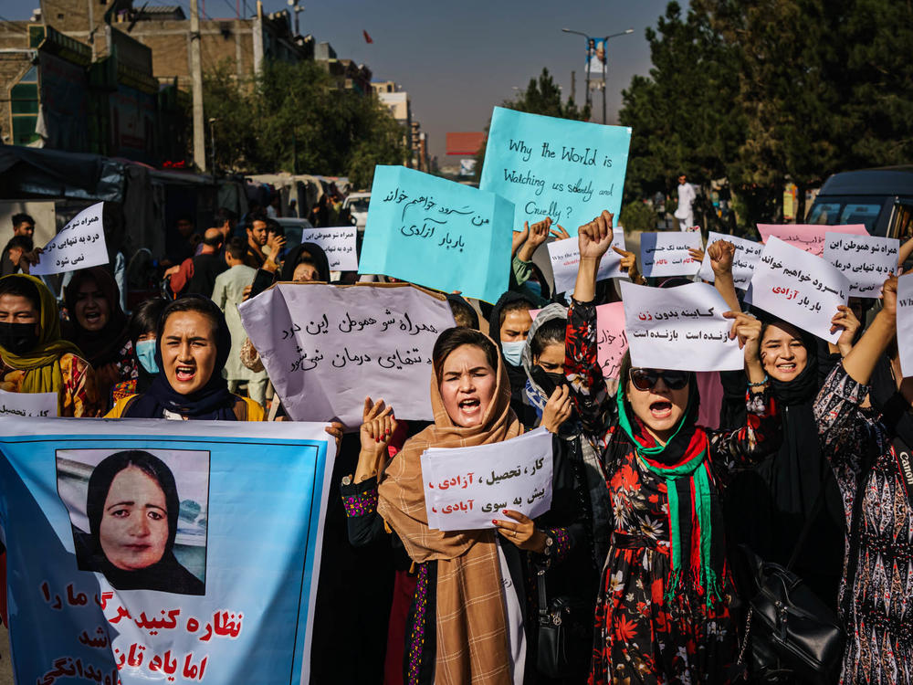 Protesters march in Kabul on Wednesday, a day after the Taliban announced their all-male interim government. At left, a protester carries a sign with a photo showing Banu Negar, a pregnant police officer who was killed in front of her relatives early this week in Ghor province. Family members accuse the Taliban of carrying out the killing.