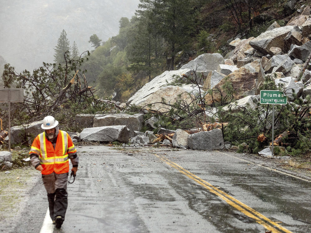 Caltrans maintenance supervisor Matt Martin walks by a landslide covering Highway 70 in the Dixie Fire zone Sunday in Plumas County, Calif. Heavy rains blanketing Northern California created slide and flood hazards in land scorched during last summer's wildfires.