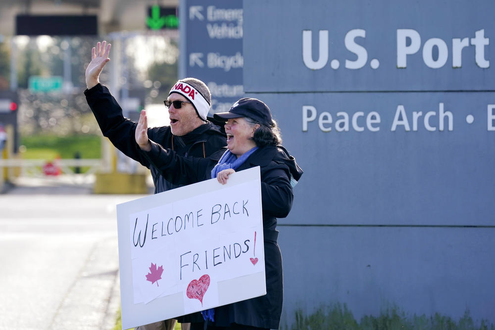 Dual U.S.-Canadian citizen Traysi Spring, right, and her American husband Tom Bakken, hold a homemade sign to welcome people heading into the U.S. from Canada on Monday.