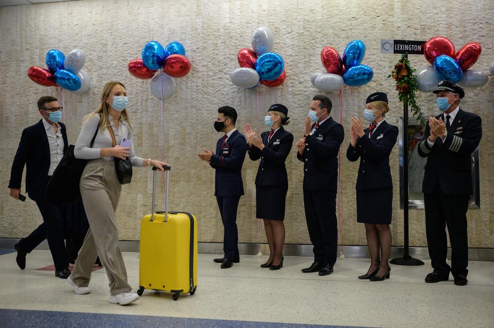 Passengers walk past airline staff as part of a welcoming event after arriving on a flight from the UK, following the easing of pandemic travel restrictions at JFK international airport in New York.