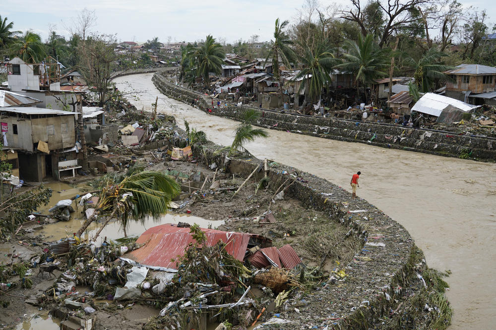 A man stands beside damaged homes along a swollen river due to Typhoon Rai in Talisay, Cebu province, central Philippines on Friday, Dec. 17, 2021.