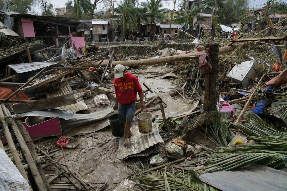 A man carries pails beside damaged homes due to Typhoon Rai in Talisay, Cebu province, central Philippines on Friday, Dec. 17, 2021.