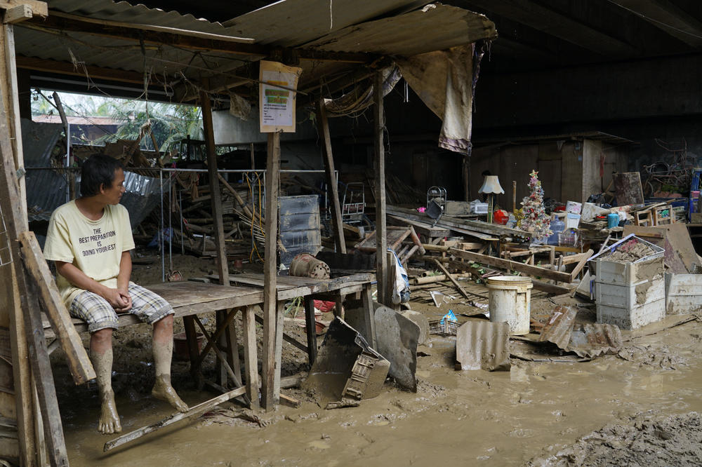A man sits beside remnants of damaged homes in Talisay city, Cebu province, central Philippines on Friday, Dec. 17, 2021.