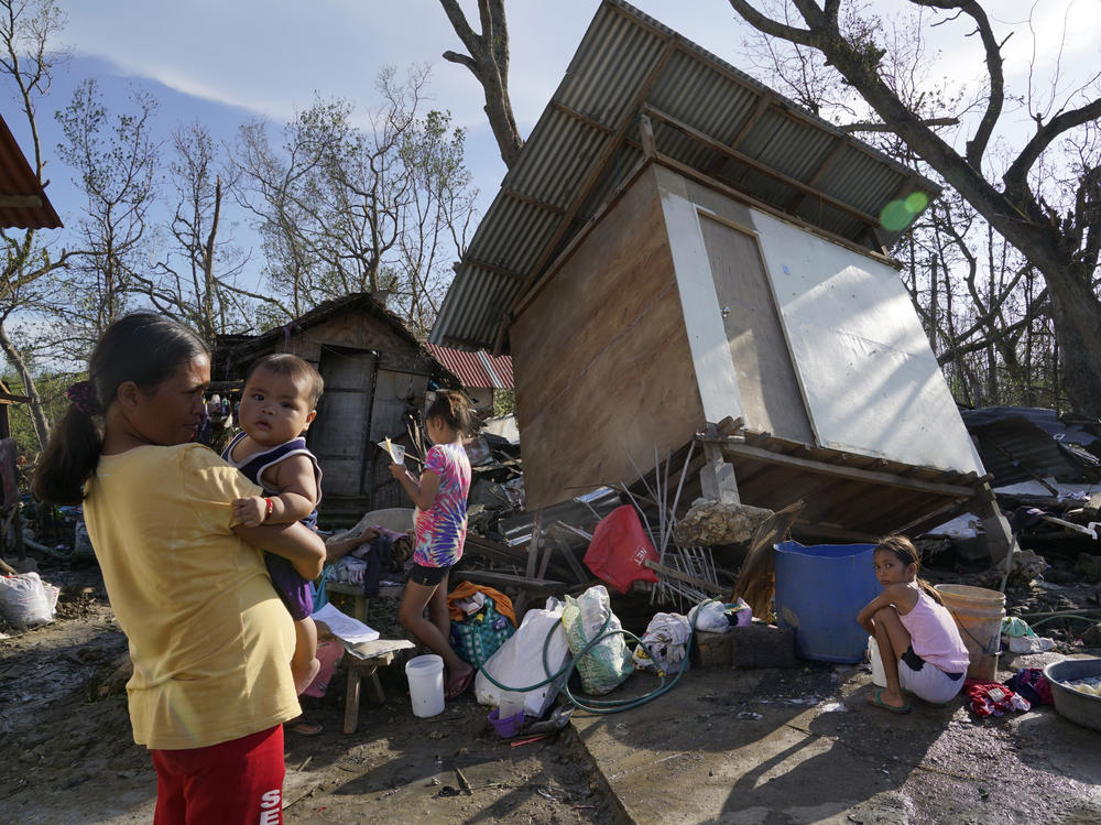 Residents stand amid damaged homes following Typhoon Rai in Talisay, Cebu province, central Philippines on Saturday, Dec. 18, 2021. The strong typhoon engulfed villages in floods that trapped residents on roofs, toppled trees and knocked out power in southern and central island provinces, where more than 300,000 villagers had fled to safety before the onslaught, officials said.