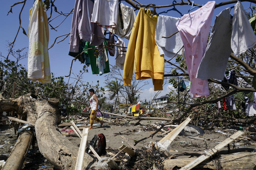 A woman walks past clothes that are left to dry on toppled trees due to Typhoon Rai in Talisay, Cebu province, central Philippines on Saturday Dec. 18, 2021.