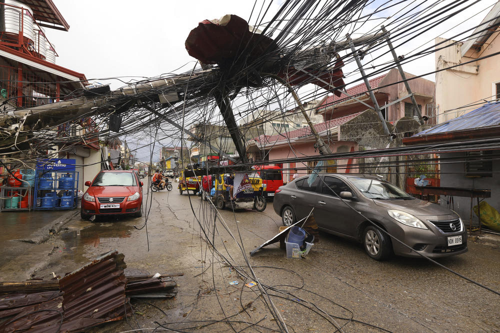 In this photo provided by Greenpeace, cars pass by a toppled electrical post due to Typhoon Rai in Surigao city, Surigao del Norte, southern Philippines as power supply remains down on Sunday Dec. 19, 2021.