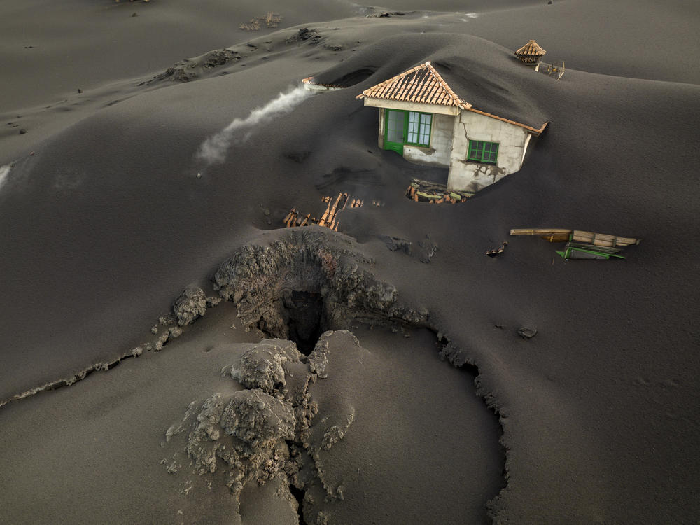 A fissure is seen next to a house covered with ash on the Canary island of La Palma on  Dec. 1. Authorities on the Spanish island are declaring a volcanic eruption that has caused widespread damage but no casualties officially finished.