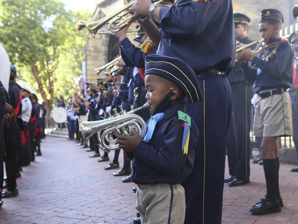 A young trumpeter joins a band for the arrival of the hearse carrying the coffin of Anglican Archbishop Emeritus Desmond Tutu at the St. George's Cathedral.