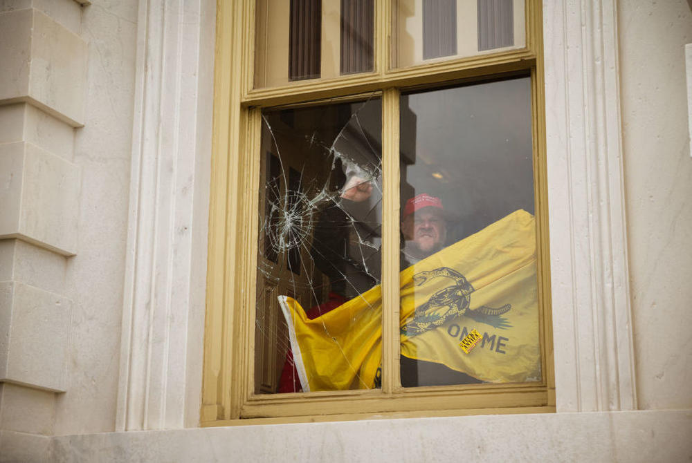 A member of a pro-Trump mob shatters a window with his fist from inside the Capitol after breaking into it on Jan. 6, 2021.