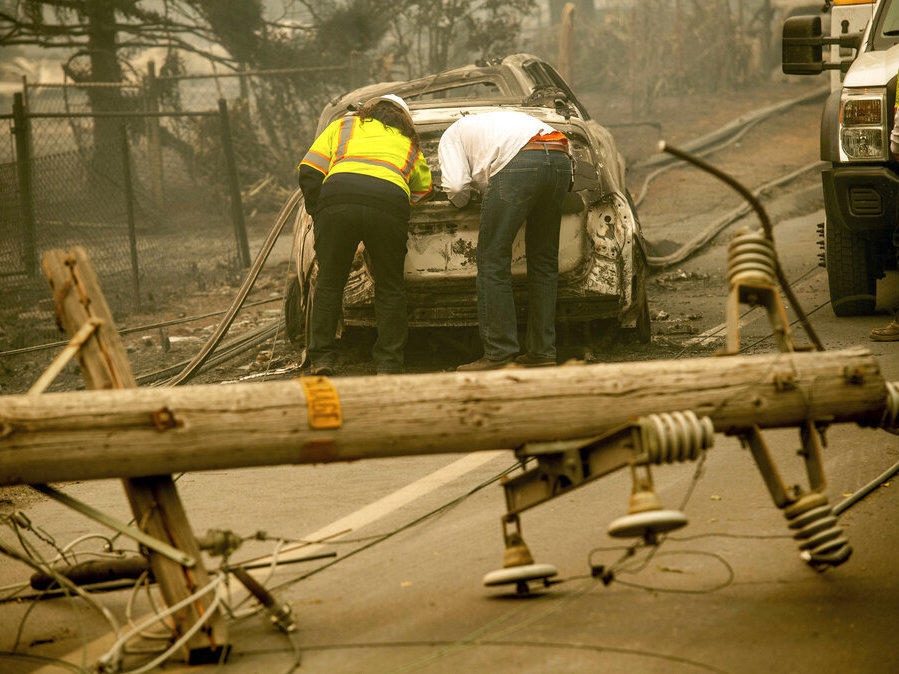 In this Nov. 10, 2018 file photo, with a downed power utility pole in the foreground, Eric England, right, searches through a friend's vehicle after the wildfire burned through Paradise, Calif.
