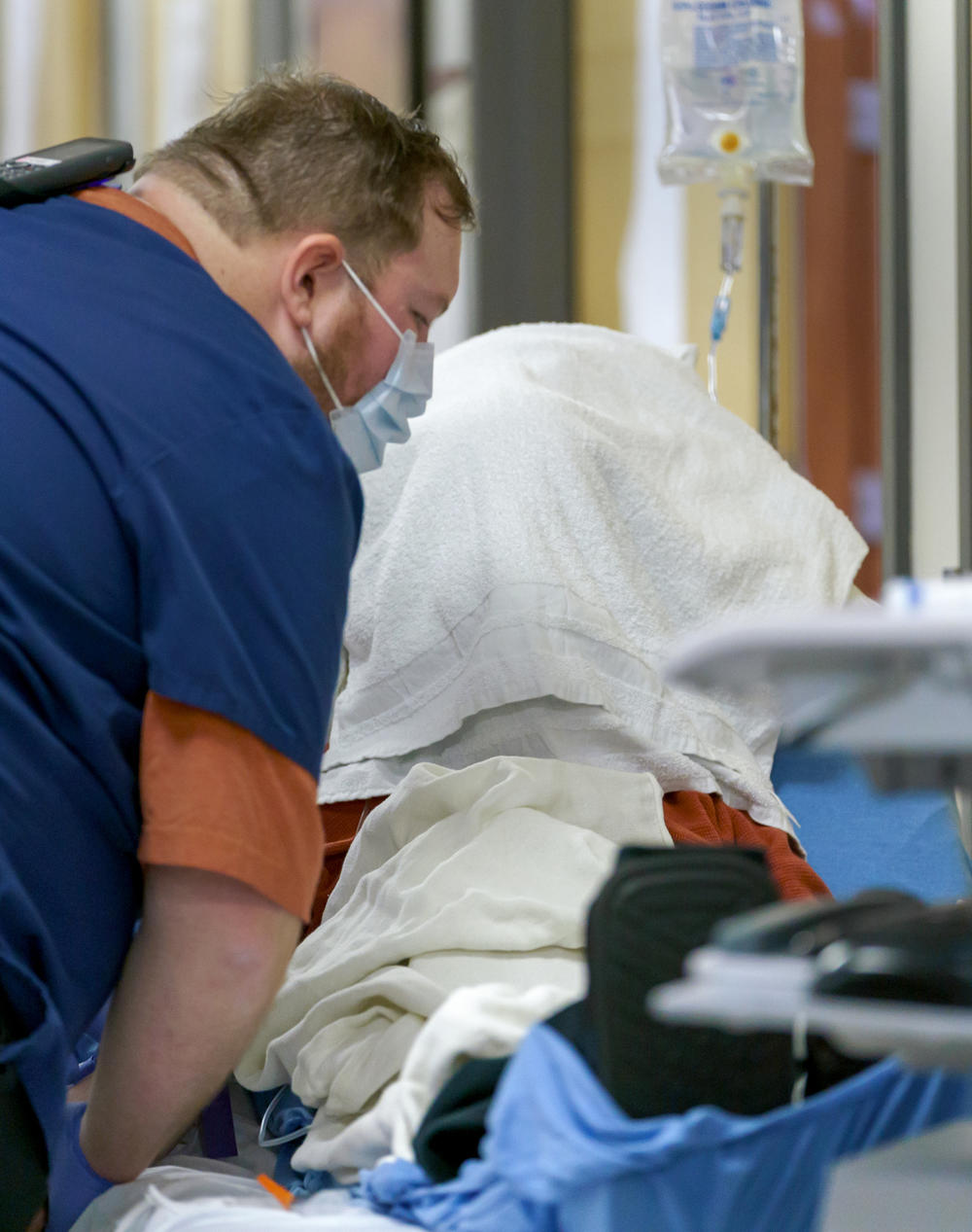 A patient covers his head with a towel while receiving fluids in the hallway of the emergency department.