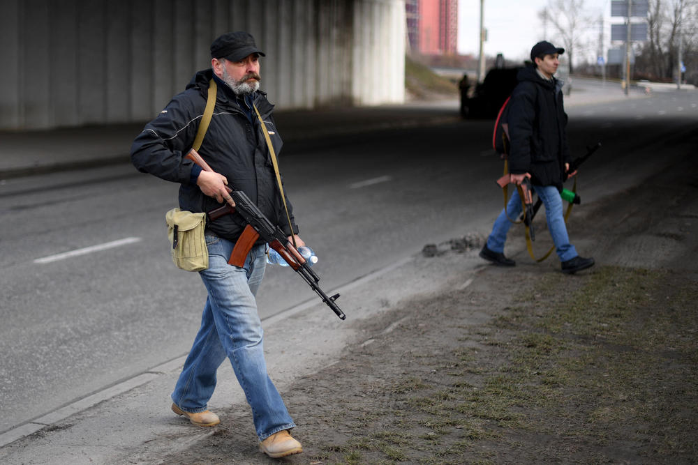 Volunteers, one holding an AK-47 rifle, protect a main road leading into Kyiv on February 25, 2022. - Ukrainian forces fought off Russian invaders in the streets of the capital Kyiv on February 25, 2022, as President Volodymyr Zelensky accused Moscow of targeting civilians and called for more international sanctions.