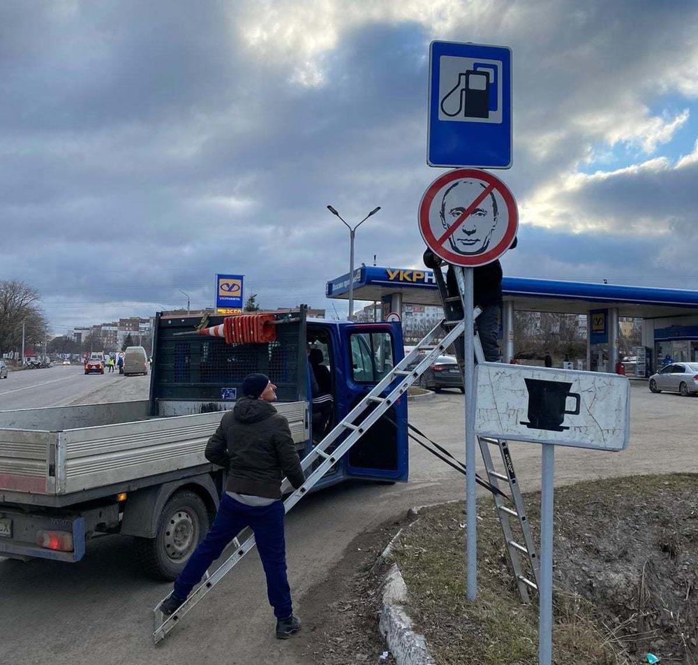 A Ukrainian road worker installs a sign featuring Russian President Vladimir Putin's face crossed out.