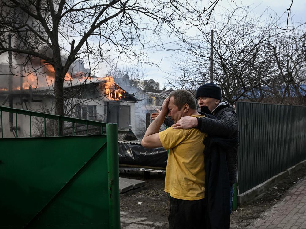Yevghen Zbormyrsky, 49, is comforted as he stands in front of his burning home after it was shelled in the city of Irpin, outside Kyiv, Ukraine, on Friday. The U.N. Human Rights Council overwhelmingly voted to create a top-level investigation into violations committed following Russia's invasion of Ukraine.