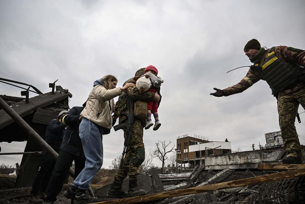 <strong>March 5:</strong> A Ukrainian serviceman carries a child while helping people to cross a destroyed bridge as they evacuate the city of Irpin, northwest of Kyiv.