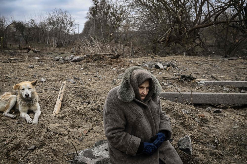 <strong>March 5:</strong> A woman sits while people cross a nearby destroyed bridge as they evacuate the city of Irpin, northwest of Kyiv.