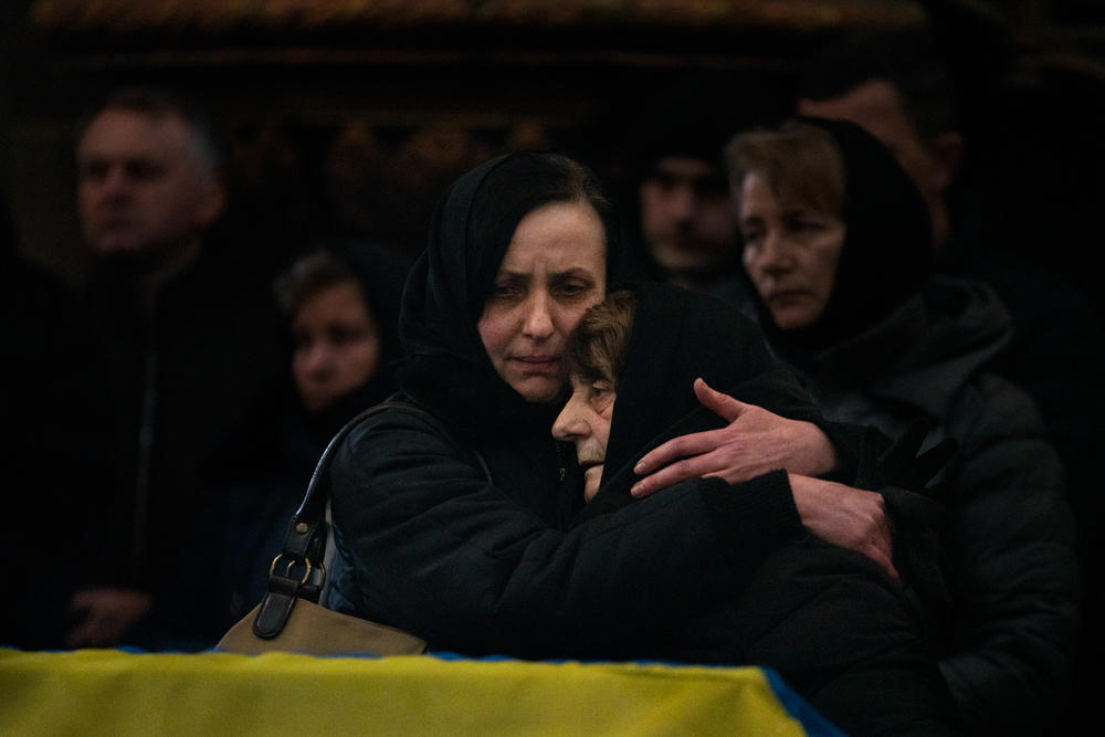 Oksana Dudar, left, the wife of Viktor Dudar, hugs her mother-in-law at her husband's funeral Tuesday in Lviv, Ukraine. Viktor was a soldier who was killed by Russian forces. A U.S. defense analyst estimates more than 1,500 were killed in the first five days of the war. The Ukrainian military tells NPR it isn't disclosing the number of soldiers lost in the fight with Russia.