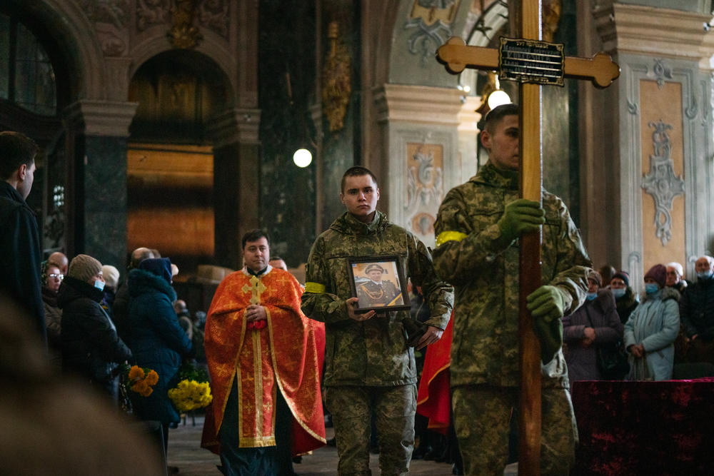 Soldiers and priests walk into the Church of the Most Holy Apostles Peter and Paul on Tuesday in downtown Lviv, Ukraine, carrying a cross and an image of Ivan Koverznev, a Ukrainian lieutenant who was killed by Russian forces on March 2.